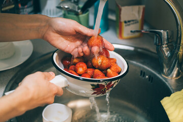 Person is washing strawberries in a sink