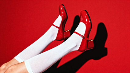 Playful fashion shot of female legs in white knee socks wearing shiny red Mary Jane heels on bold red background, strong shadows and retro party vibe, generative AI