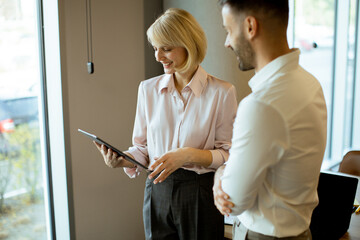 Two professionals exchange ideas while using a tablet in a modern office