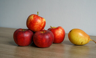 Autumn still life - fresh ripe red apples and one ripe yellow pear on a wooden table