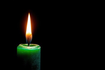 A vibrant, green candle burns against a stark black backdrop, casting a warm glow