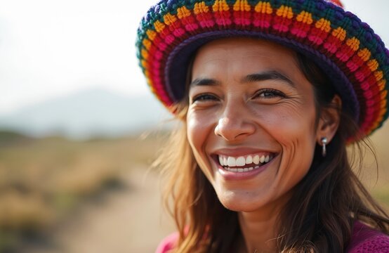 Close-up face of smiling woman wearing colorful Peruvian chullo hat. Detailed knit pattern visible on hat. Outdoor setting with blurred background. Joyful expression, warm eyes.