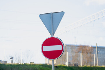 Red circular no entry symbol mounted on post with unused triangular frame overhead in outdoor transit zone illustrating regulated direction control and roadway prohibition marker placement