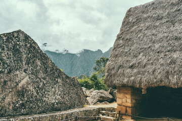 Sacred Rock carved stone monument and a thatched roof house at the Historic Sanctuary of Machu Picchu, Peru