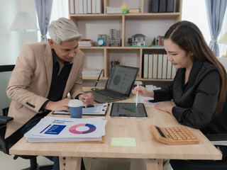 Two Asian colleagues working happily on laptop and financial documents. Professional man and woman. Cooperation and business partnership concept.