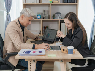 Naklejka premium Two Asian colleagues working happily on laptop and financial documents. Professional man and woman. Cooperation and business partnership concept.