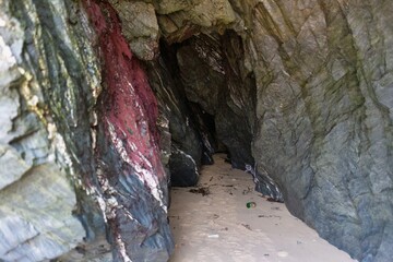 A cave on a beach. The cave's rock face has streaks of pink, adding a unique charm in Polly Joke - Cornwall - UK