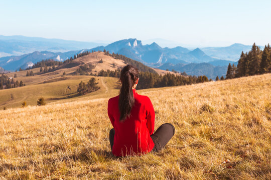 A young girl sits on the ground and looks at the beautiful panorama of autumn mountains