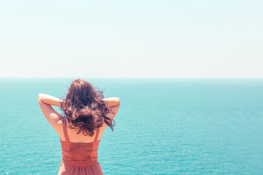 Young girl in dress looking at turquoise seascape and enjoying summer vacation