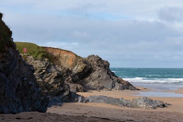 Rocky beach with sand leads to the ocean, partially cloudy sky in the background in Polly Joke - Cornwall - UK