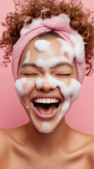 Obraz premium A joyful person laughs with cleansing foam covering the face against a pink background. 