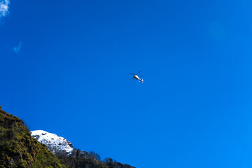 Helicopter in the Sky Above a Green and Snowy Mountain Slope