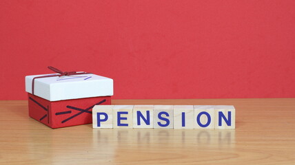 The word pension written on wooden cubes, on a red background a gift package with a bow.