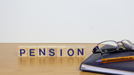 The word pension written on wooden cubes, on the desk with glasses and a diary.