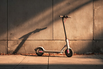A scooter stands on the sidewalk in the sunset light.