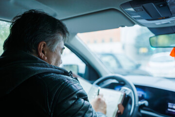 Man writing in notebook while sitting in car