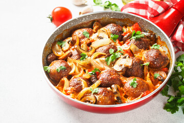Meatballs with mushrooms in tomato sauce in a frying pan.