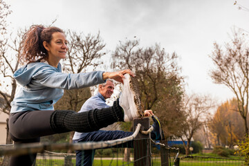 Senior couple stretching legs on a fence, finding personal fitness in a park