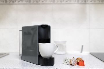 Modern single-serve capsule coffee machine brewing espresso into a white cup on a kitchen counter with scattered coffee pods.
