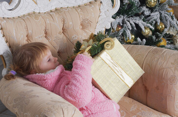 a little girl in a pink sweater is sitting in a chair and being handed a large box wrapped in Christmas paper