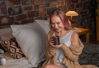 A young woman in a knitted sweater sits in the bedroom in the evening