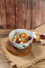 Fototapeta premium Flavorful Herbal Soup: A steaming bowl of nourishing herbal soup, rich with medicinal ingredients and a hint of jujube sweetness, served on a rustic wooden surface, promising warmth and well-being.