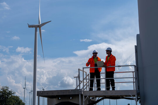 Workers conduct safety checks at a wind farm on a clear day under a blue sky