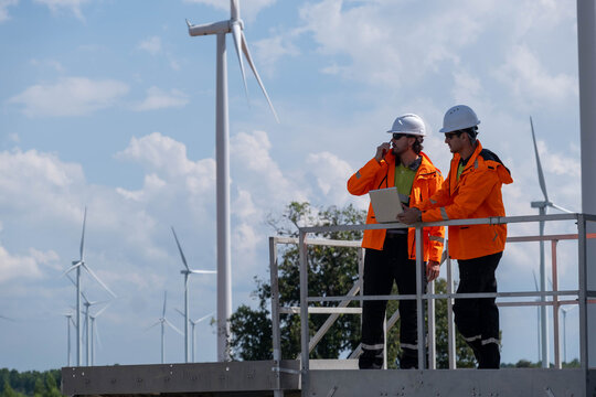 Wind farm technicians inspect equipment and review data at a renewable energy site during a sunny day