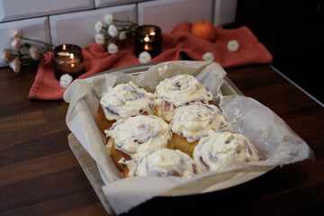 Cinnamon rolls covered with cream in baking trays in the kitchen