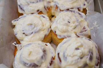 Cinnamon rolls covered with cream in baking trays in the kitchen