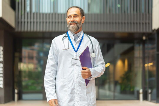 Experienced male doctor smiling carrying medical clipboard