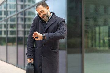 Mature businessman talking on phone checking smartwatch