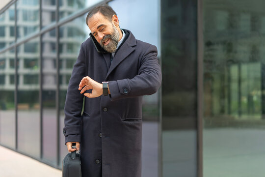 Mature businessman talking on phone checking smartwatch