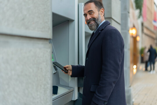 Mature man making contactless payment with smartphone at atm