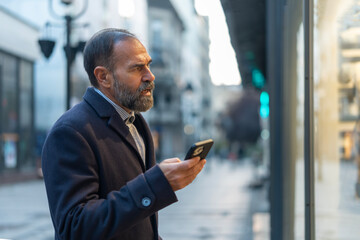 Mature man checking smartphone looking at shop window