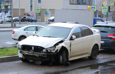 A white, damaged car after an accident stands on the street, Pyatiletka Avenue, Saint Petersburg,...