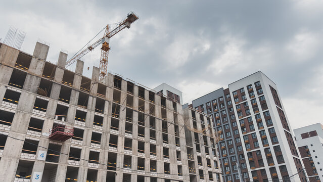Construction site with a high-rise building under development and a tower crane against a cloudy sky, concept of urban growth, architecture, real estate, and infrastructure development