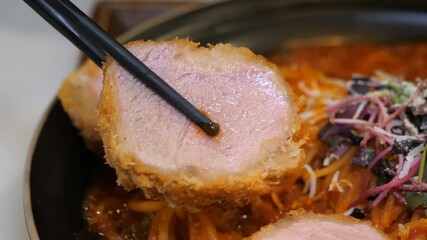 A close up shot of hands using chopsticks to dip a piece of breaded pork cutlet into sauce, followed by lifting a mouthful of red sauce spaghetti