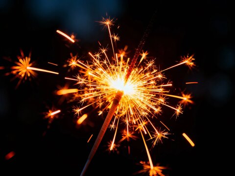Close-up of a lit sparkler emitting bright sparks against a dark background - Powered by Adobe