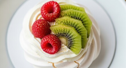 Close up overhead view of a delicate white meringue pavlova dessert topped with fresh bright red raspberries and vibrant green sliced kiwi fruit