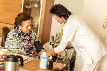 Home care nurse checking blood pressure of an elderly woman during a routine visit