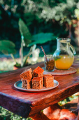 Un plato con porciones de bizcochuelos de harina integral sobre la mesa rústica con un tereré de fondo en el jardín, merienda tradicional de Paraguay y Misiones.