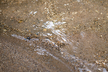 A close-up view of clear water flowing over wet, textured sand and small pebbles on a riverbank