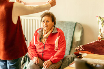 Woman assisting senior with light fitness device to support mobility and prevent contractures