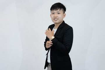 A focused young Asian professional adjusting a wristwatch on their sleeve, conveying a sense preparation, or time management against a clean white studio background
