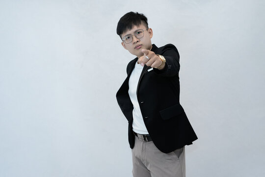 A determined and assertive young Asian professional or student wearing a blazer and glasses, standing and pointing directly at the camera in studio background