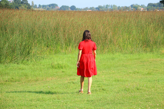 woman in red dress walking through greenery