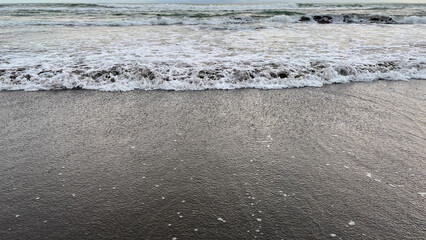 a gentle ocean wave washing over a dark sandy shore, creating foam patterns and textured water. natural beach scene with calm movement and simple composition