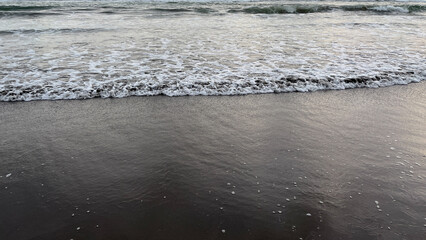a gentle ocean wave washing over a dark sandy shore, creating foam patterns and textured water. natural beach scene with calm movement and simple composition