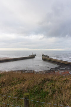 Whitby Harbor Entrance &mdash; Twin Stone Piers, Beacon Marker, and Calm Sea Under Overcast Sky